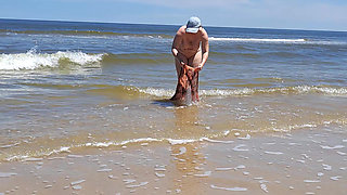Amateur filming. A nudist plays with waves on the ocean shore.