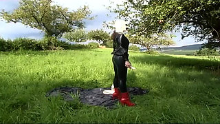 Fetish slave in latex walks and sucks a dildo on the grass